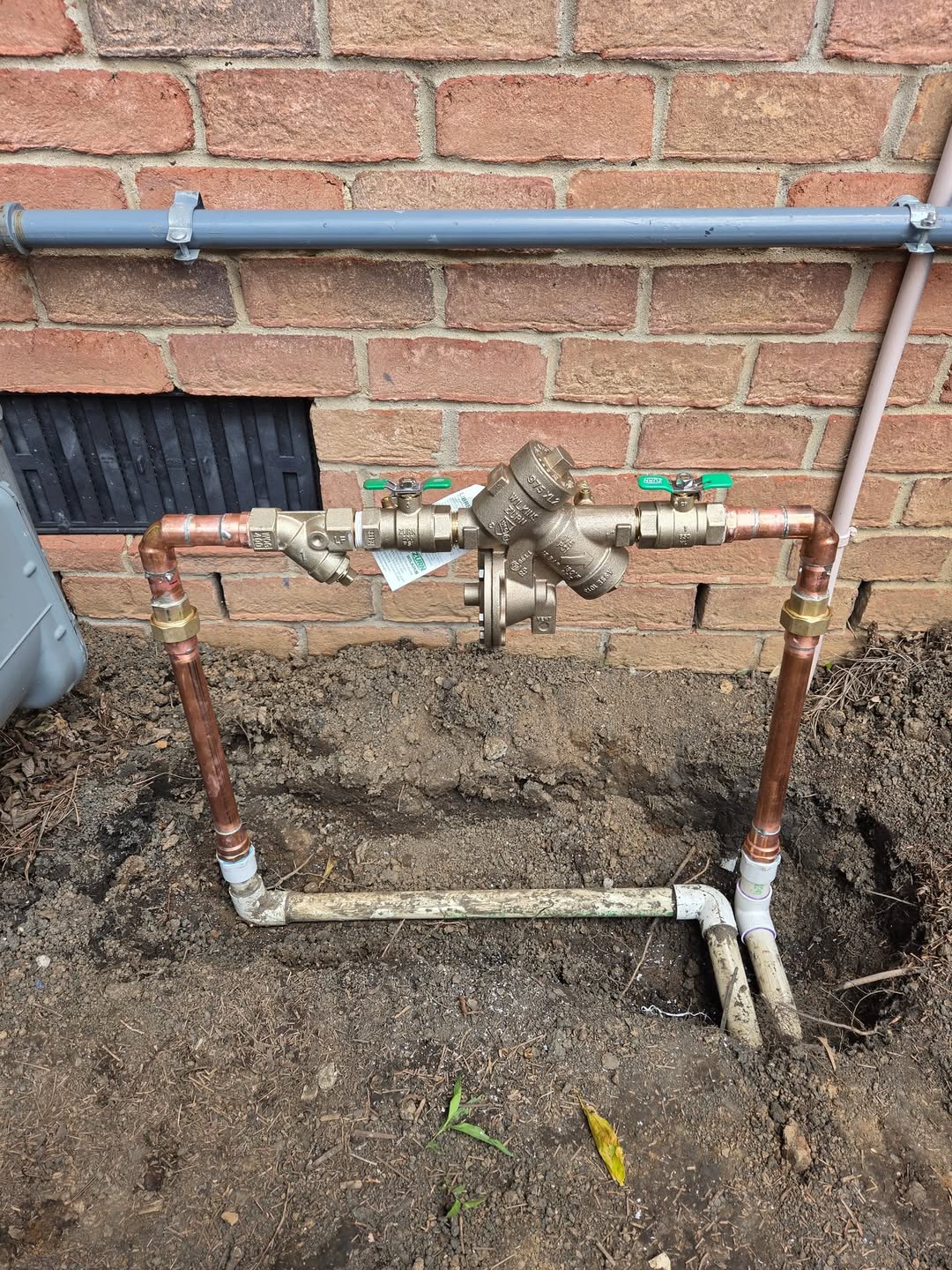 New irrigation backflow assembly with copper piping installed beside a brick building